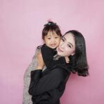 A joyful mother holding her smiling daughter against a pink backdrop, capturing love and happiness.